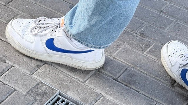 A low top pair of white Nike AF1 shoes with a blue Nike swoosh.